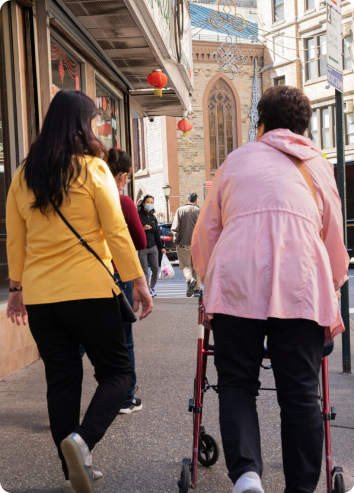 An elderly woman with a walked and a family member walk down a busy street