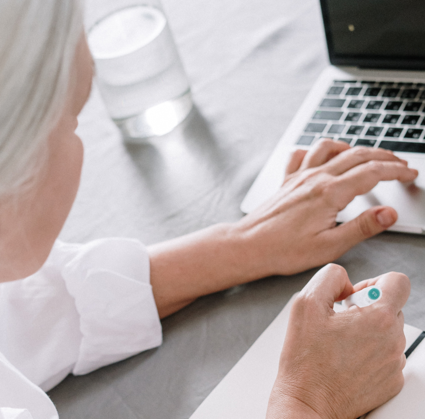 A physician uses a laptop and has a hand poised to take notes in a notebook