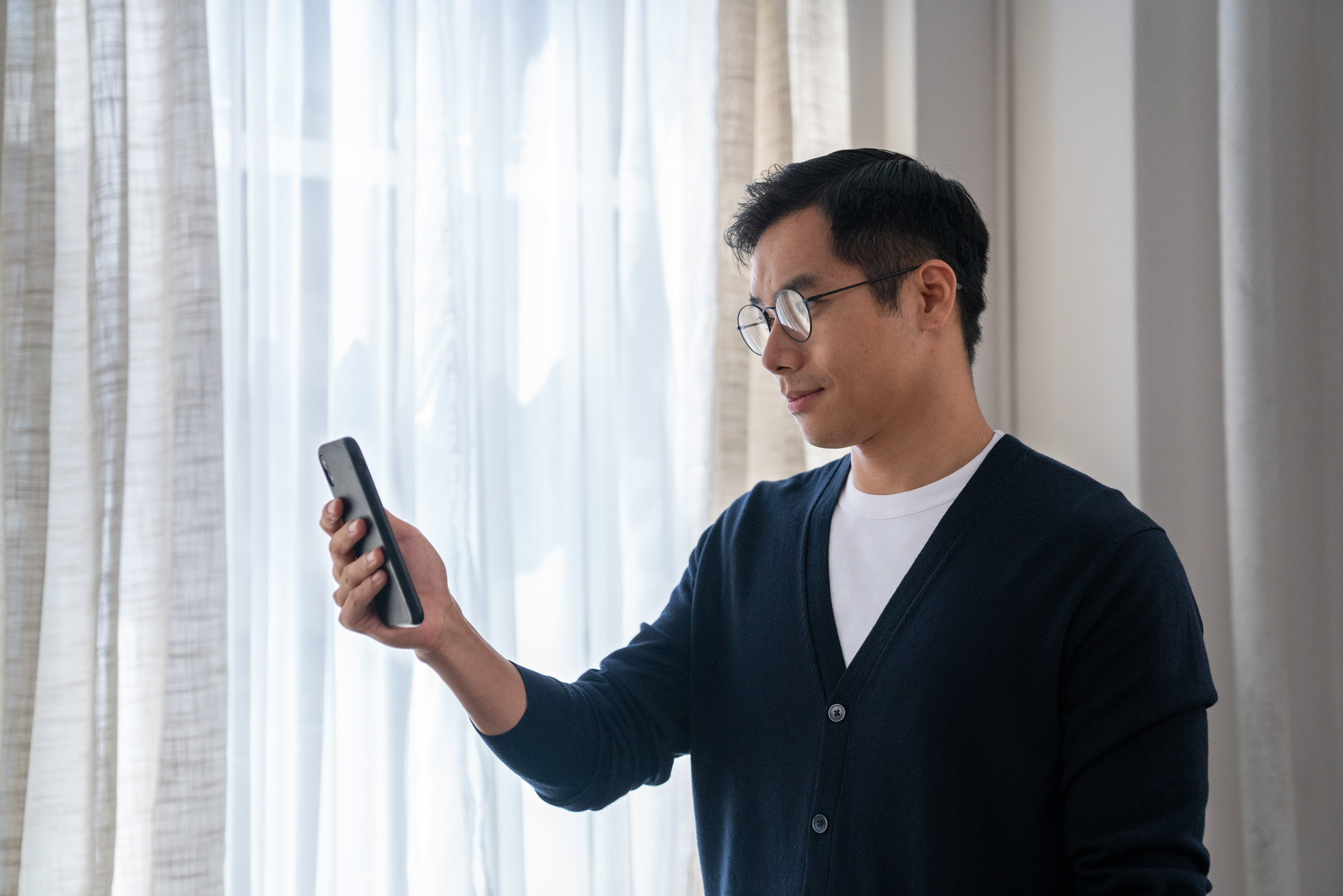 A man indoors holds up his cell phone and looks at the screen