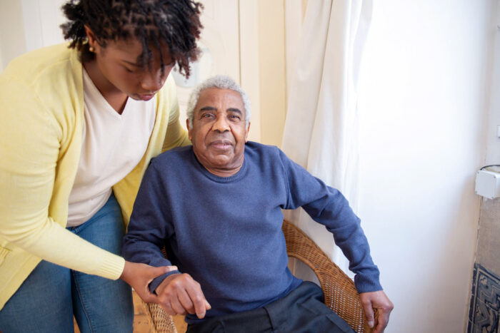 Older man helped into a chair by a family member