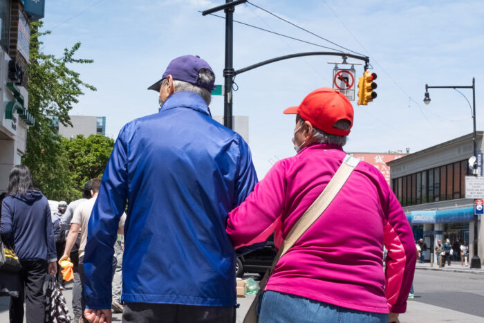 Elderly couple walking arm in arm down a busy block