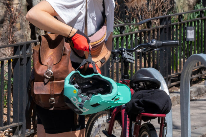 Person holding a bike helmet in front of their bike which is leaning against a bike rack
