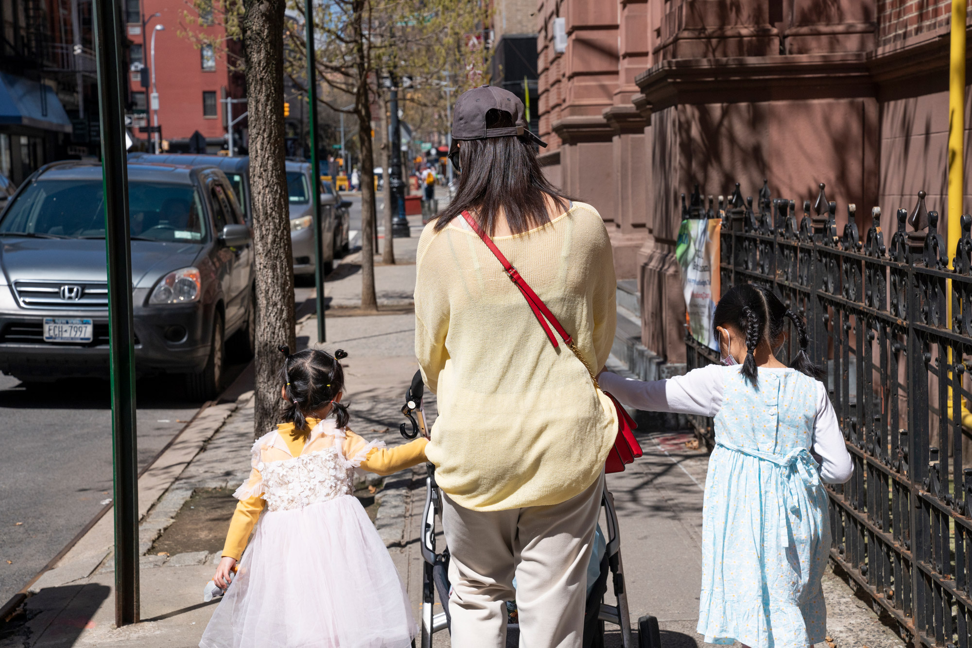 A mother and her two young daughters push a stroller down the sidewalk