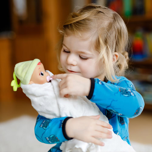 A toddler carefully holds a swaddled baby doll