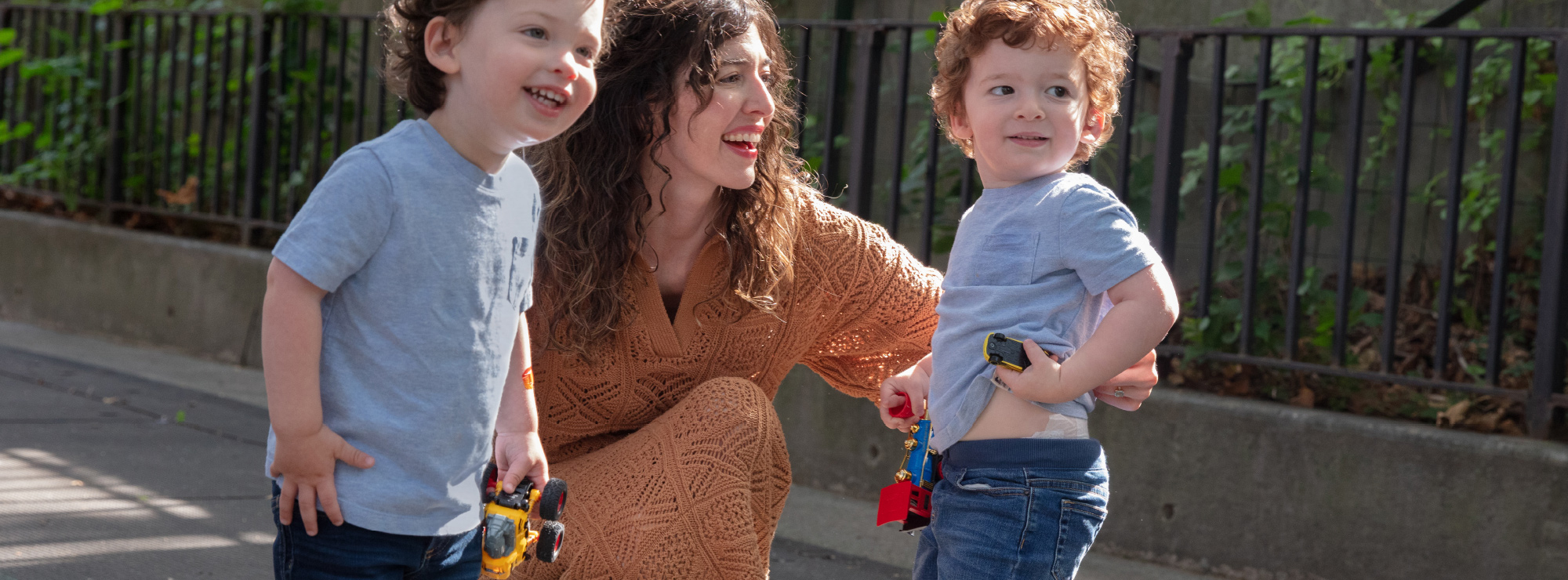 A mother smiles with her two toddlers while outside at a park