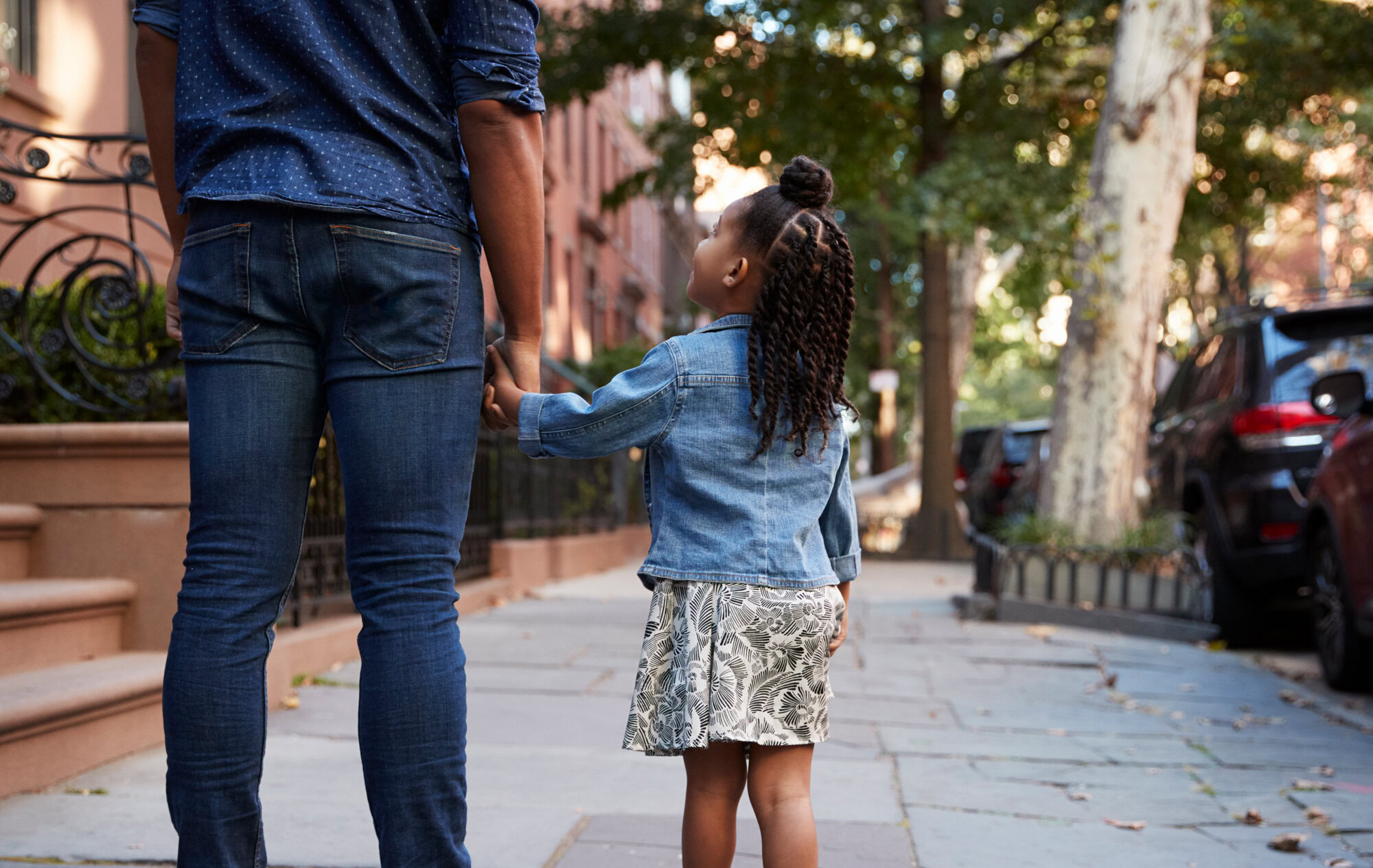 Parent and young child holding hands and walking on a New York City sidewalk