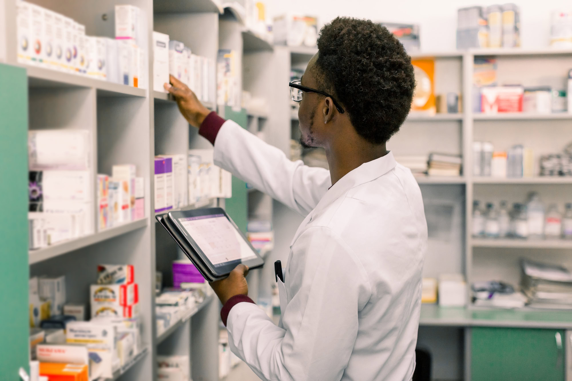 African American male pharmacist using digital tablet during inventory in pharmacy.