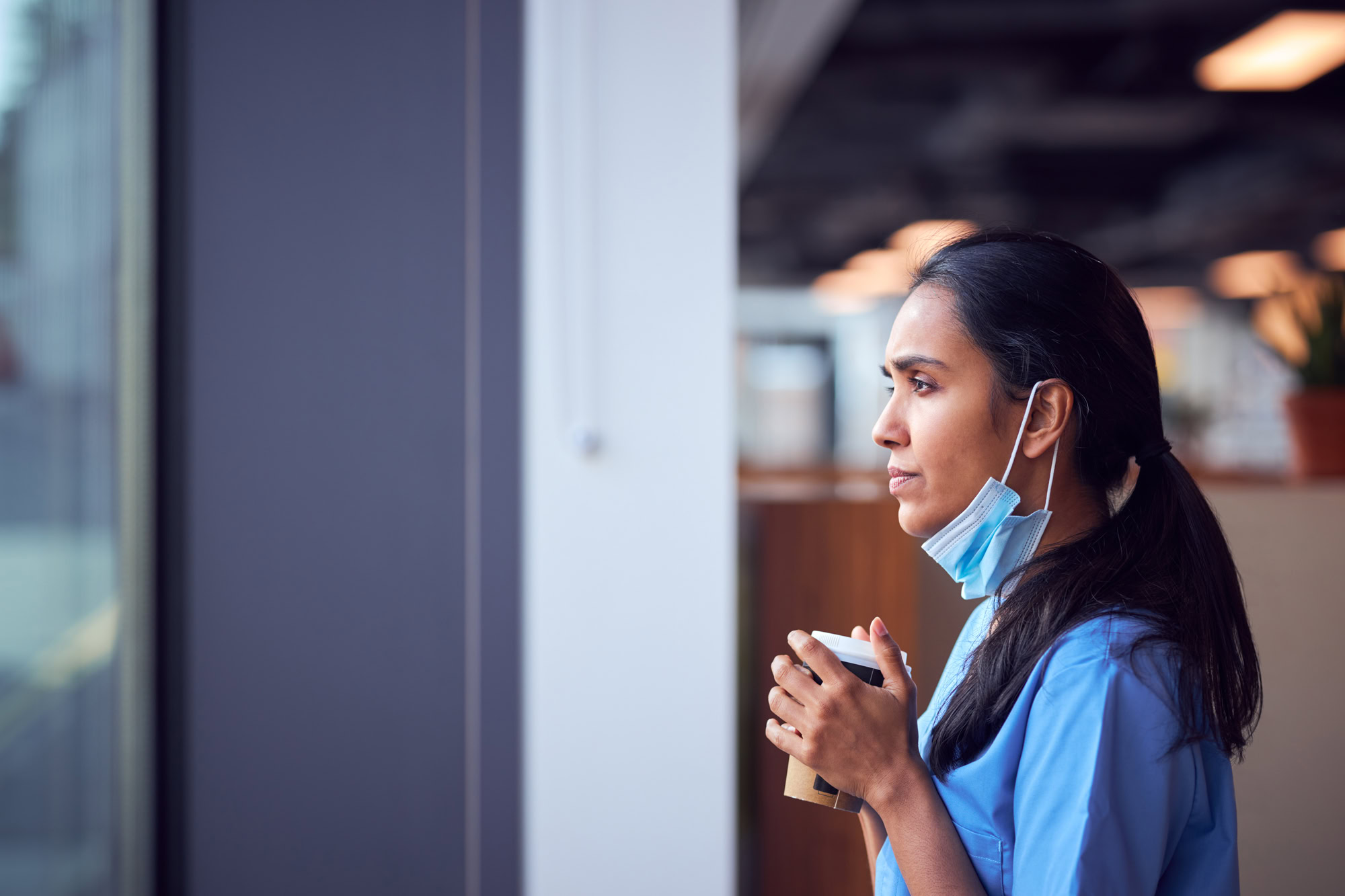 Overworked Nurse In Scrubs With Face Mask Takes Coffee Break In