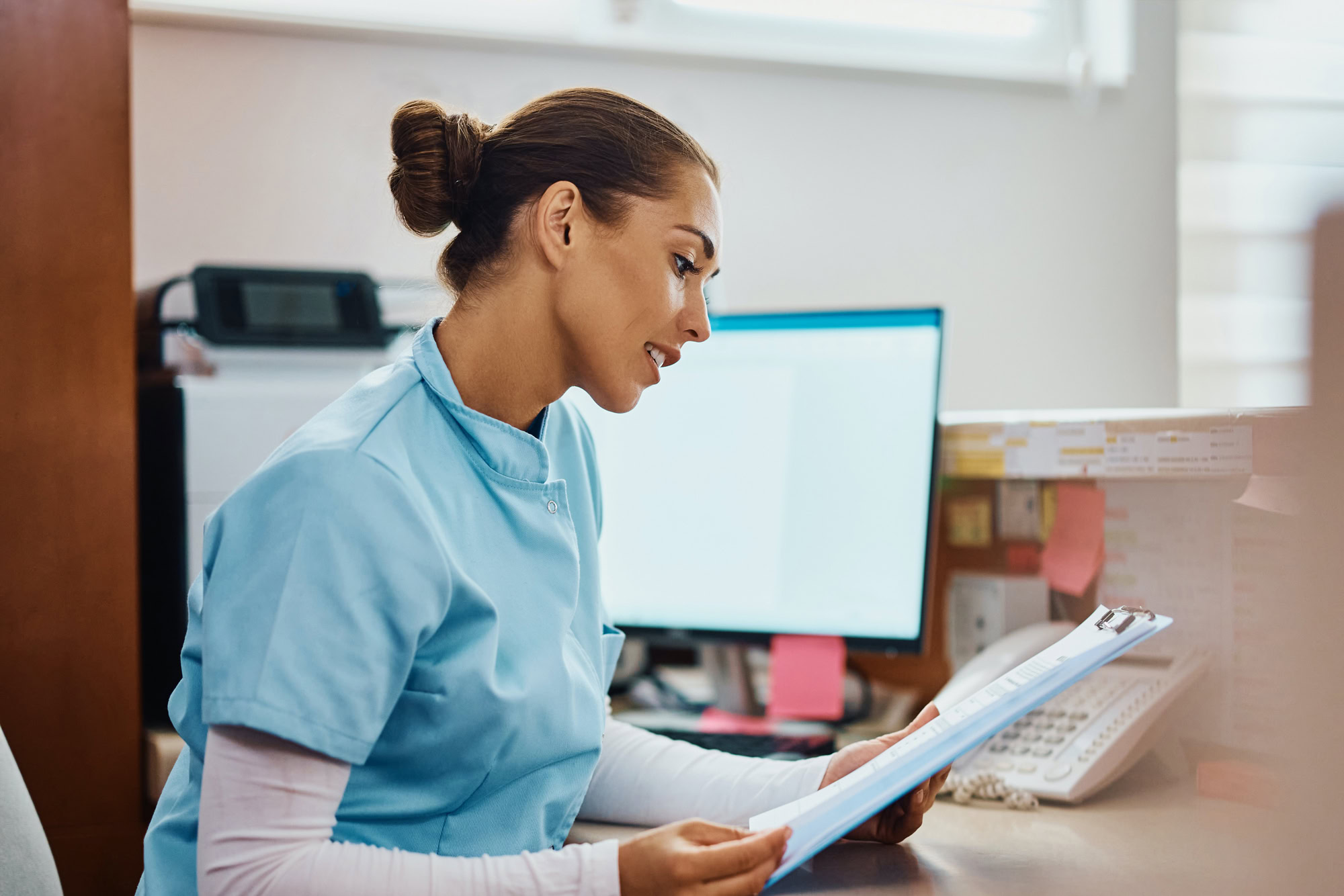 Doctor filling out MetroPlusHealth provider initial application forms on a desk with laptop and paperwork.