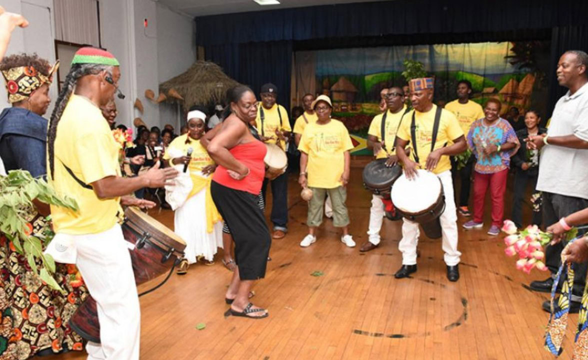 A lively group of men and women singing, dancing, and clapping during a traditional Guyanese Kwe Kwe Night celebration.