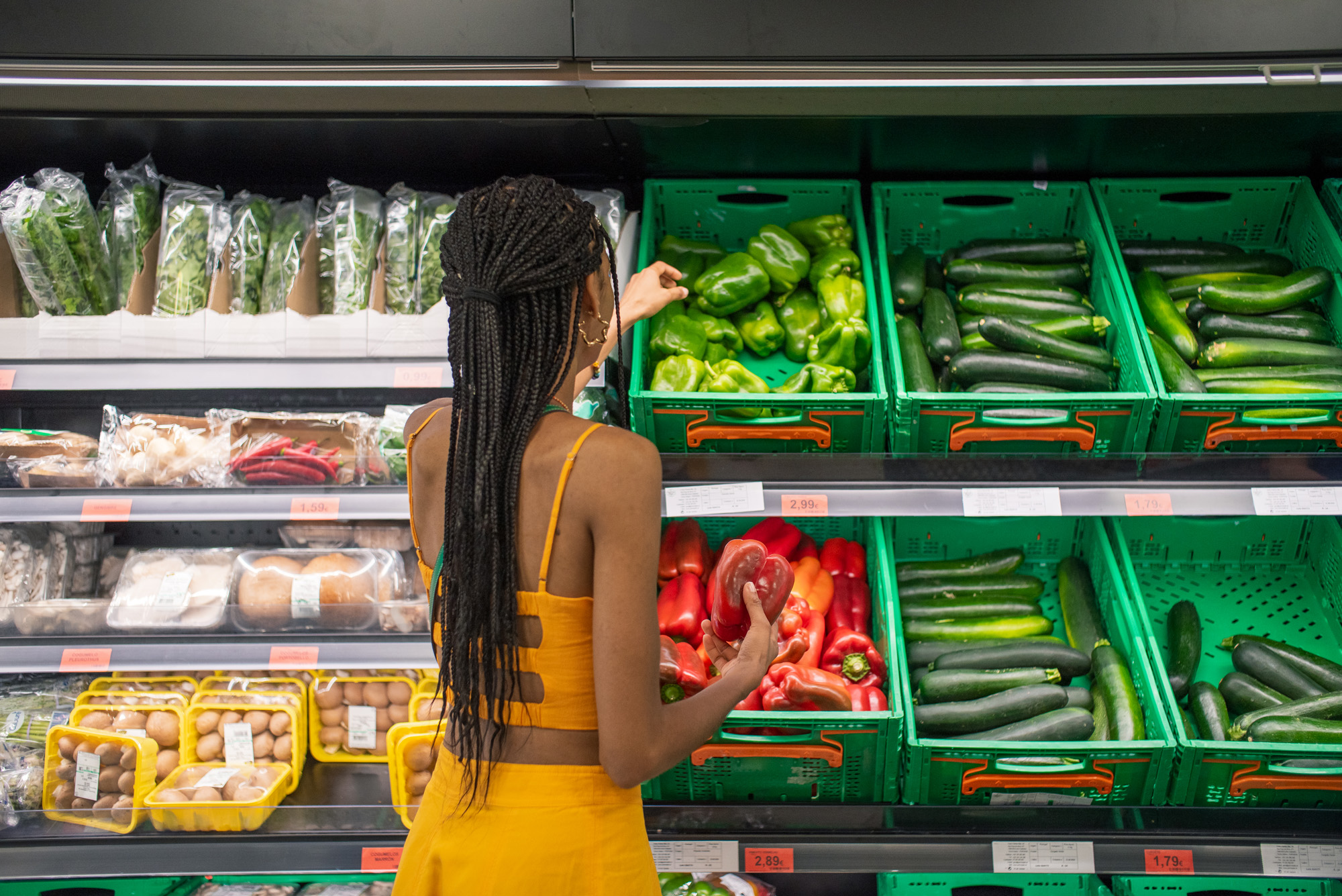 Customer picking peppers from grocery store refrigerator in vertical boxes